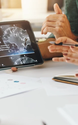 Business professionals using a tablet displaying digital analytics and global data visualizations, representing business intelligence, automation, and digital transformation.