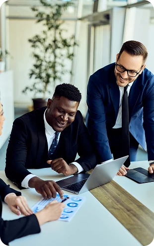 Business professionals collaborating around a laptop during a team meeting, reviewing documents and discussing business strategy in a modern office.