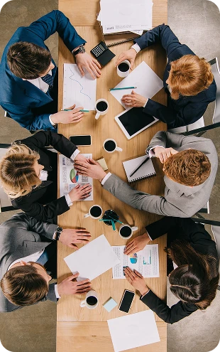 Overhead view of business professionals collaborating around a conference table, reviewing reports, sharing ideas, and planning business strategy during a team meeting.