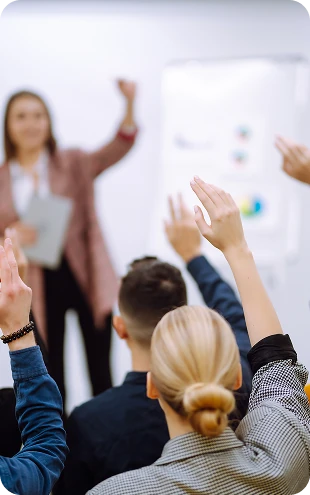 Participants raising their hands during a corporate training session while a presenter leads a workshop, representing employee engagement, learning, and professional development.